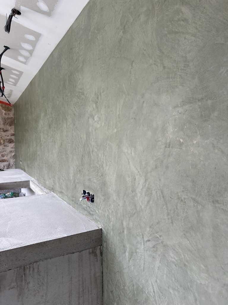 Mur de salle d'eau en tadelakt vert d'eau, au-dessus d'un plan de toilette en béton